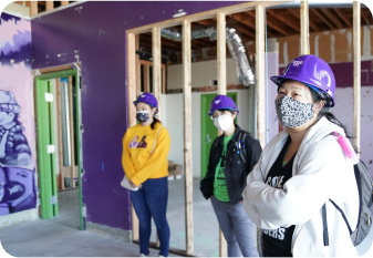Three members wearing purple hard hats that says RYSE standing inside a building that’s being renovated