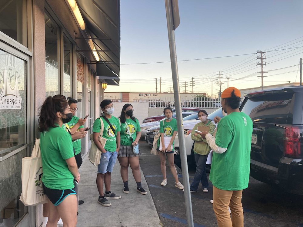 A group of canvassers in green shirts stand in a circle in a parking lot in Los Angeles