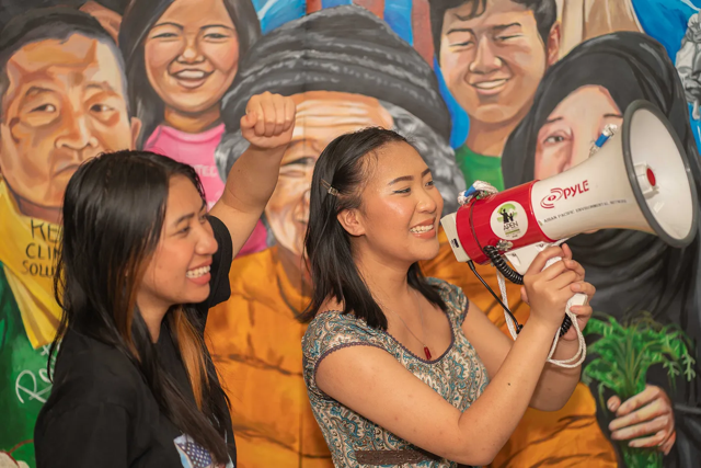 Ashley (left) and Alida Phuthama (right) hold a megaphone up in front of the newly painted mural. Photo by Denny Khamphanthong.